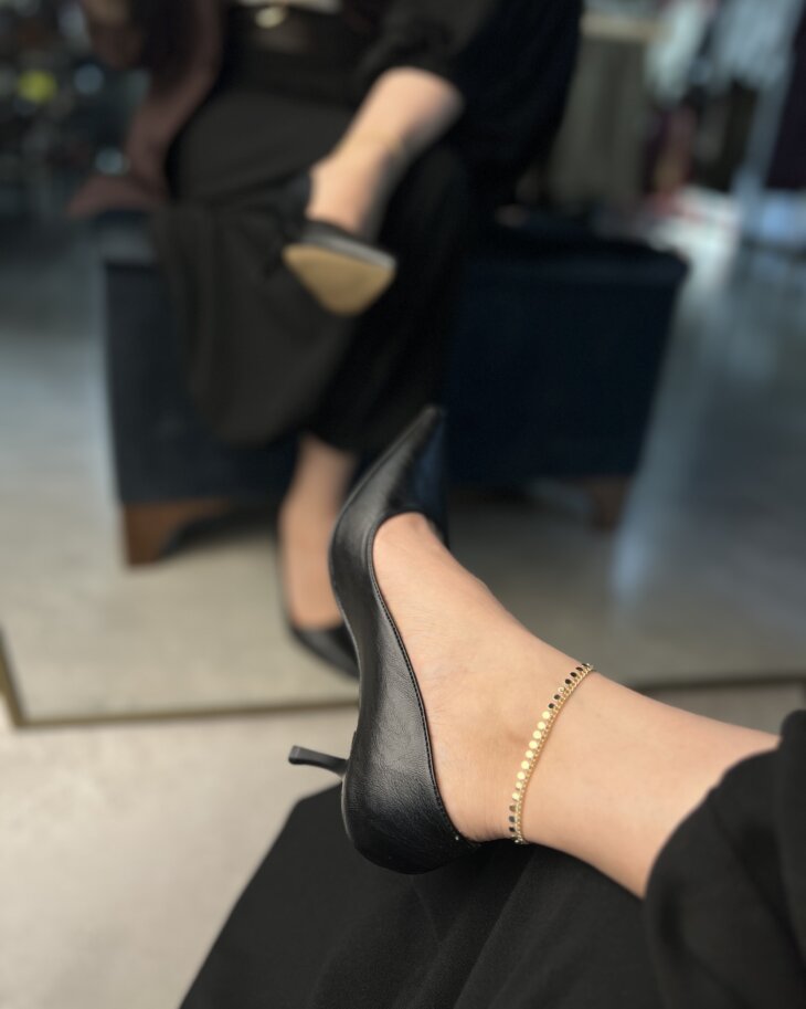Siyah stiletto ayakkabı ve zarif ayak bileği zinciri detayları.