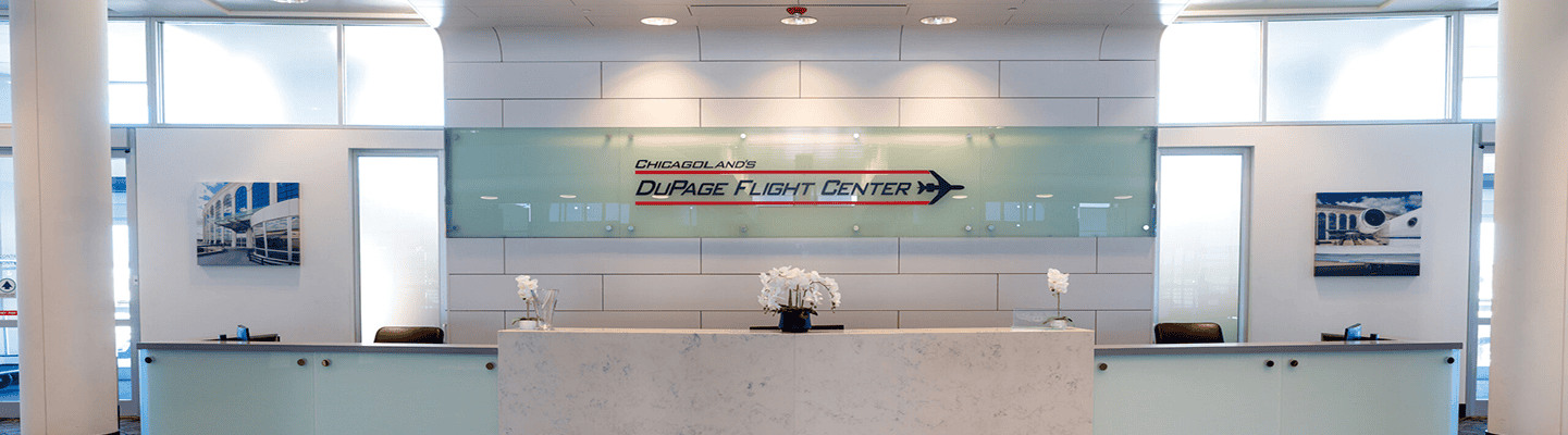 A modern, brightly lit reception area with a large central desk, a 'DuPage Flight Center' sign on a glass panel, and two smaller desks with airplane-themed artwork on the walls.