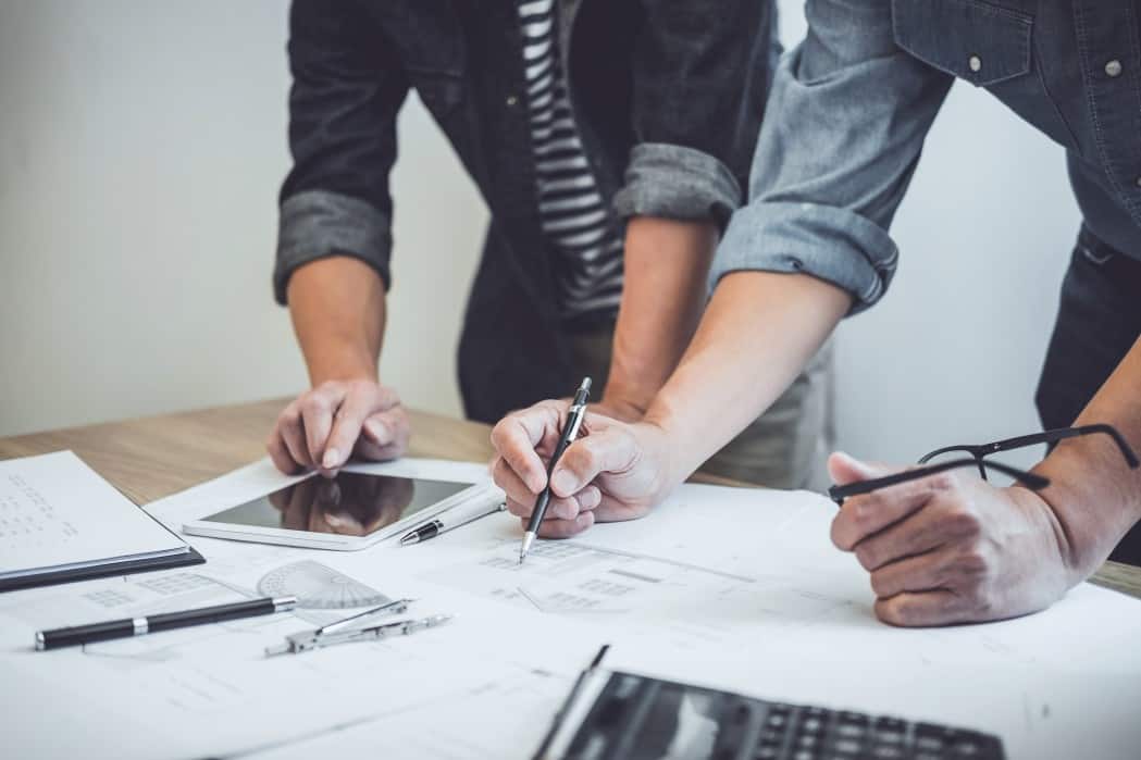 close up of hands drawing a blue print and holding glasses