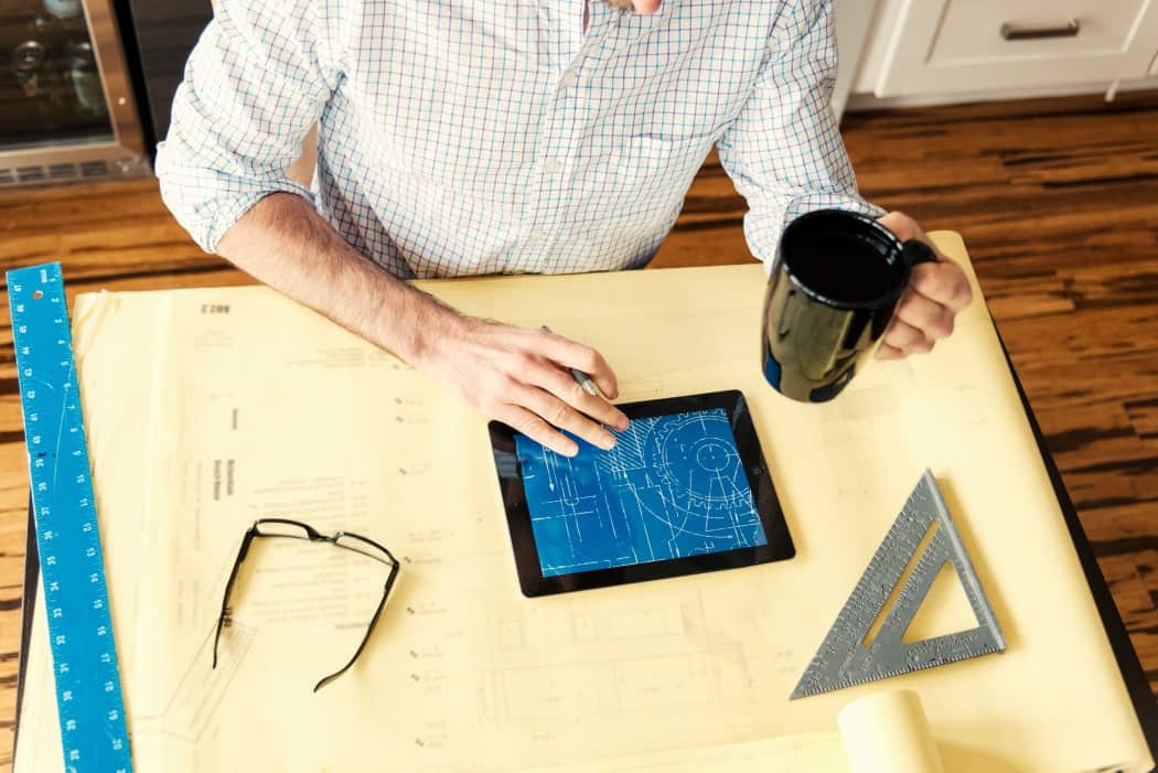 person holding coffee while working on a blueprint on an iPad