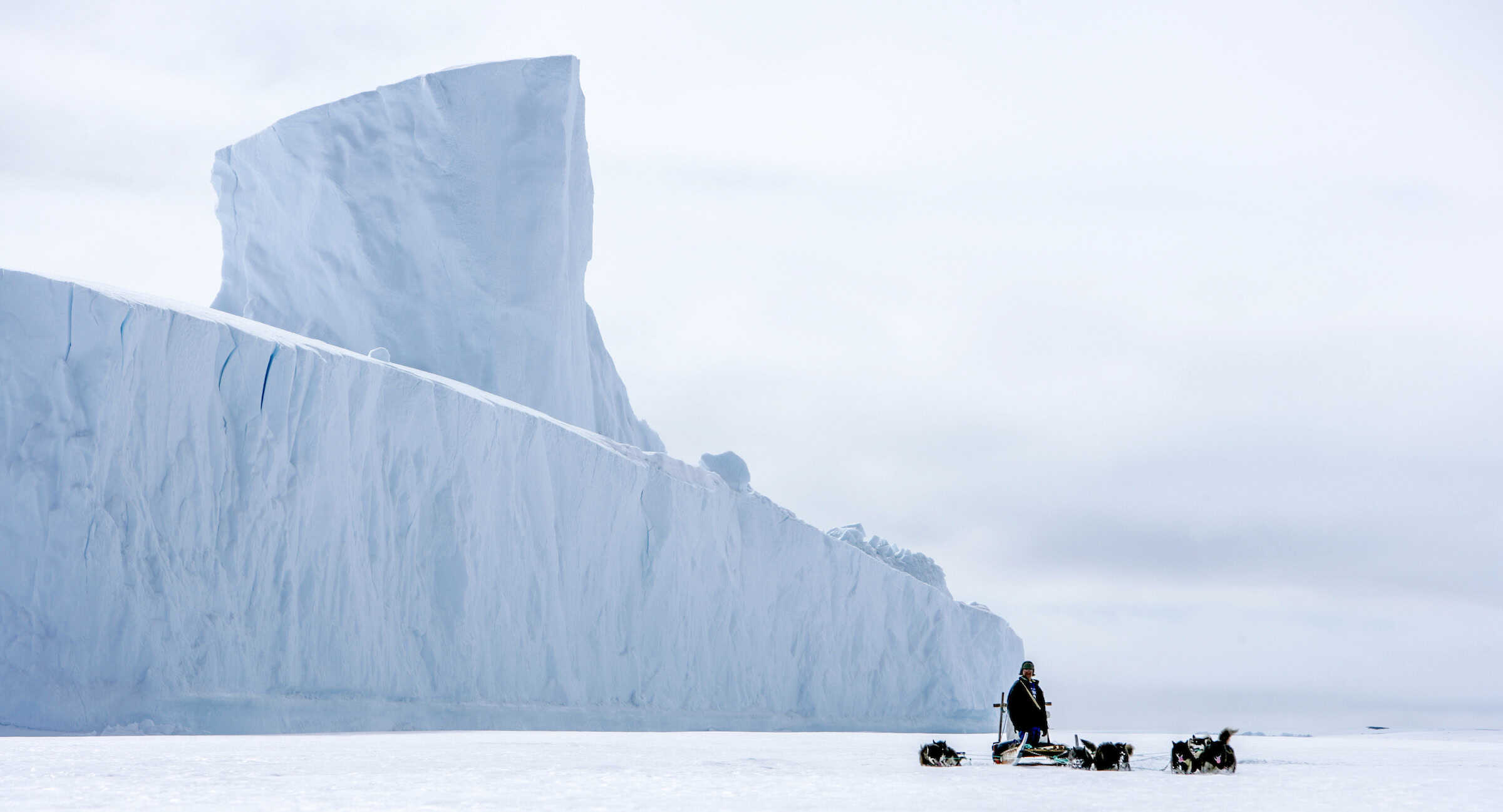Ittoqqortoormiit dog sled near large iceberg. Photo by Jørgen Chemnitz - Visit Greenland