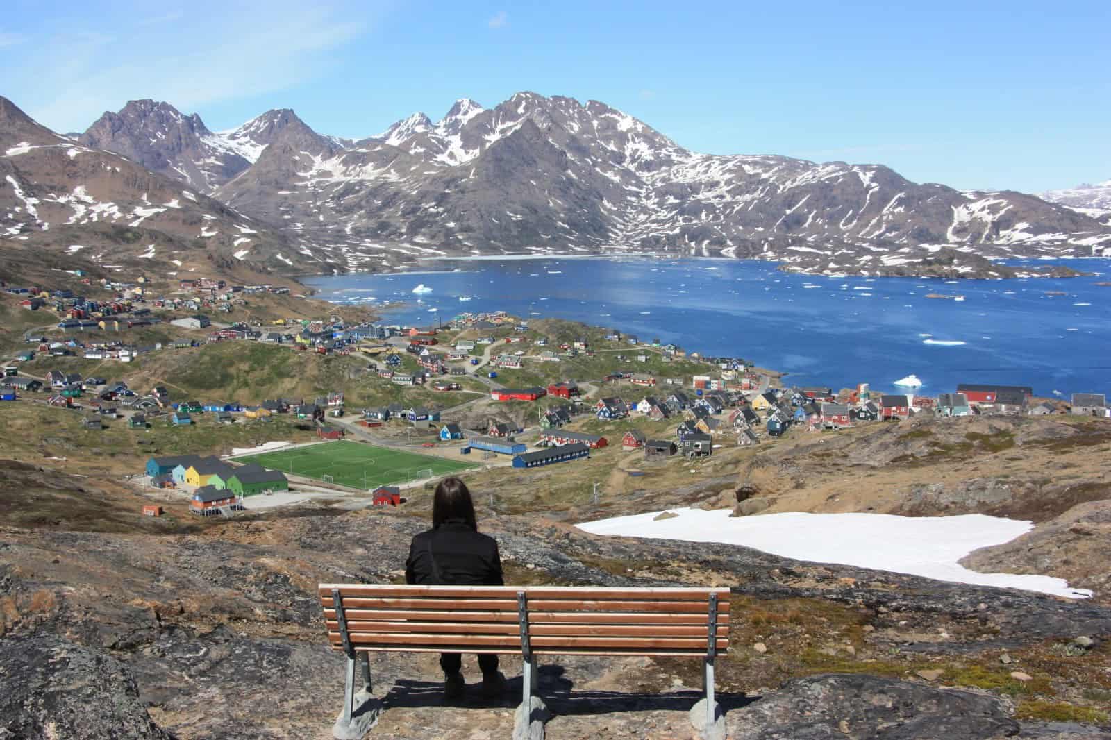 A tourist enjoying panoramic view over Tasiilaq with the big football field, fjord and mountain ranges.