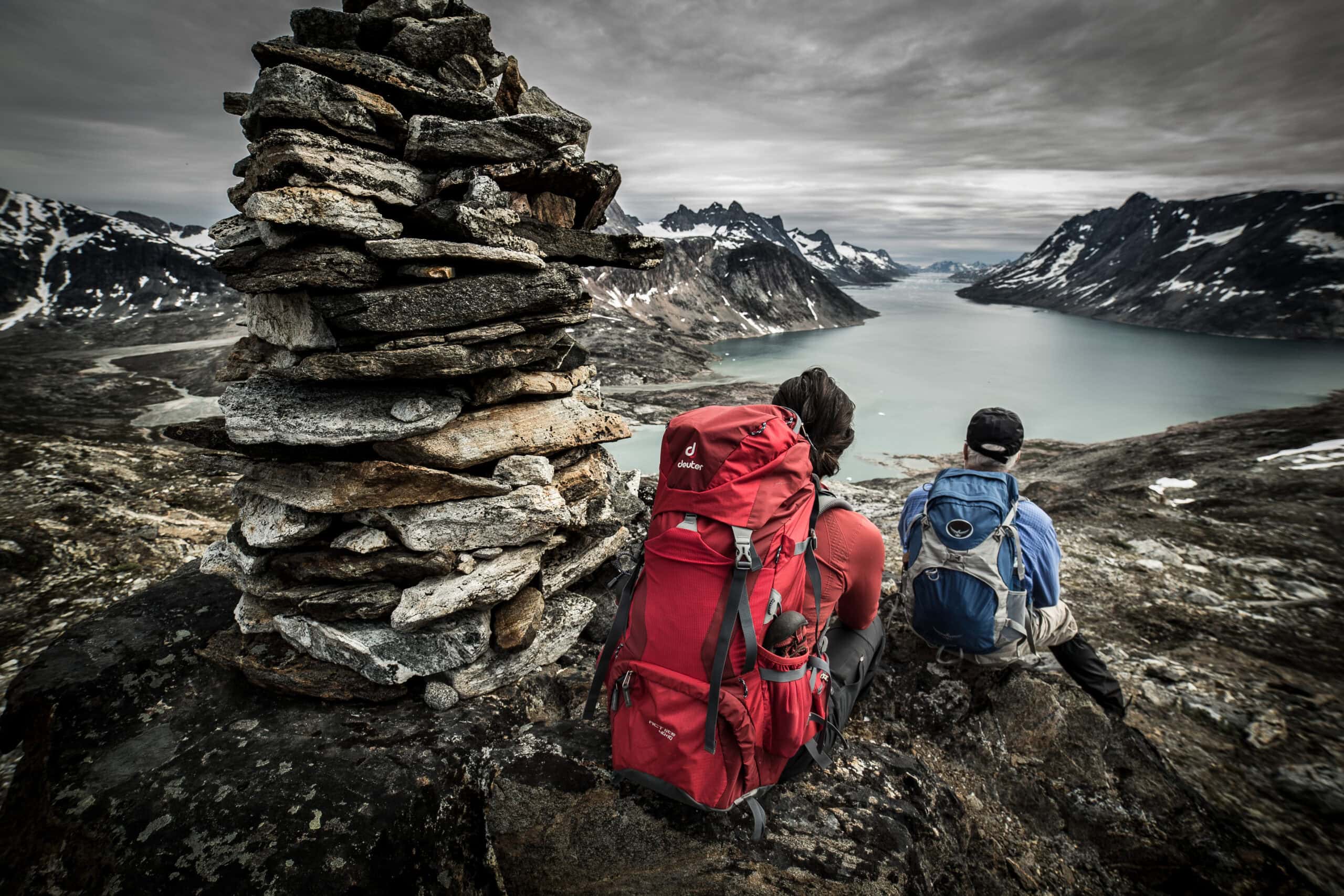 Two hikers on a Greenland Travel trek by a cairn overlooking Ikaasatsivaq sound in East Greenland near Tiniteqilaaq. Photo by Mads Pihl - Visit Greenland
