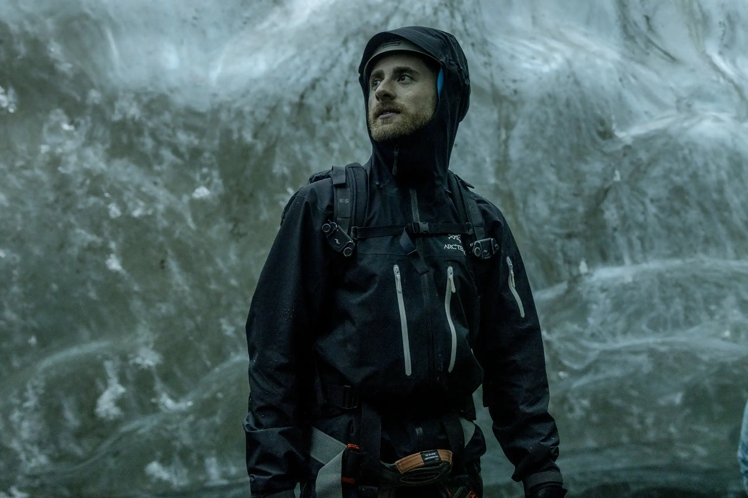 Explorer wearing technical gear inside an ice cave in East Greenland, standing against an icy backdrop.