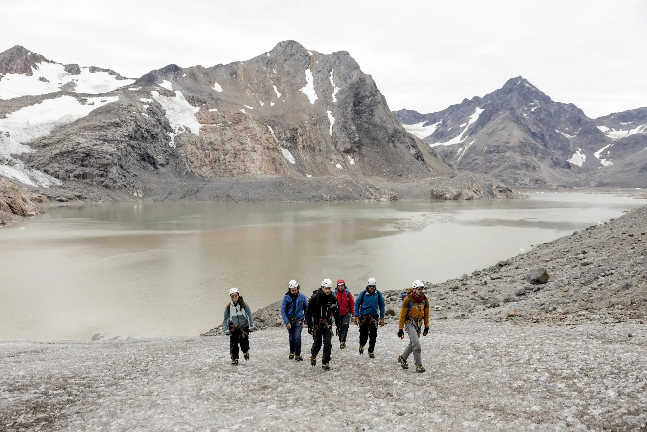 Group of hikers trekking across a glacier in East Greenland with mountains and a lake in the background.