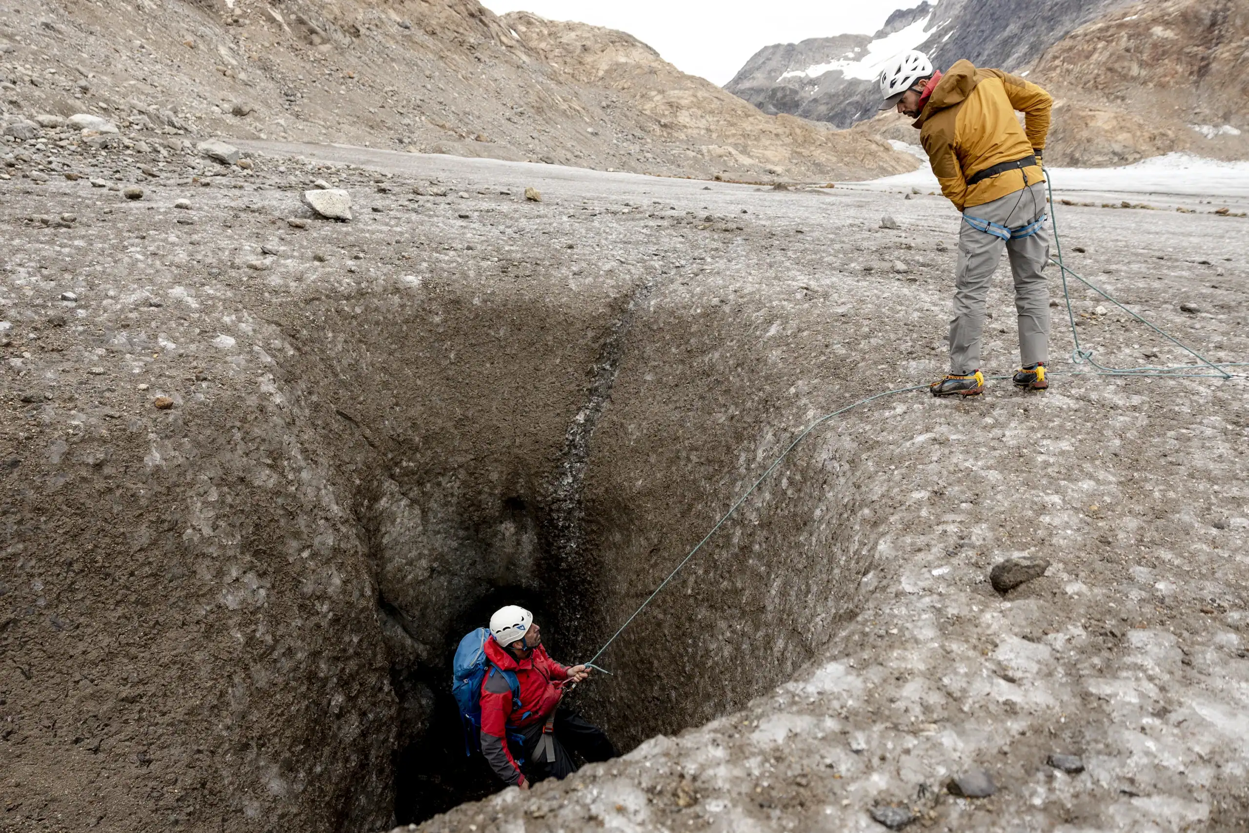 Two explorers practicing crevasse rescue on a glacier in East Greenland, one descending into a crevasse while the other holds the rope.