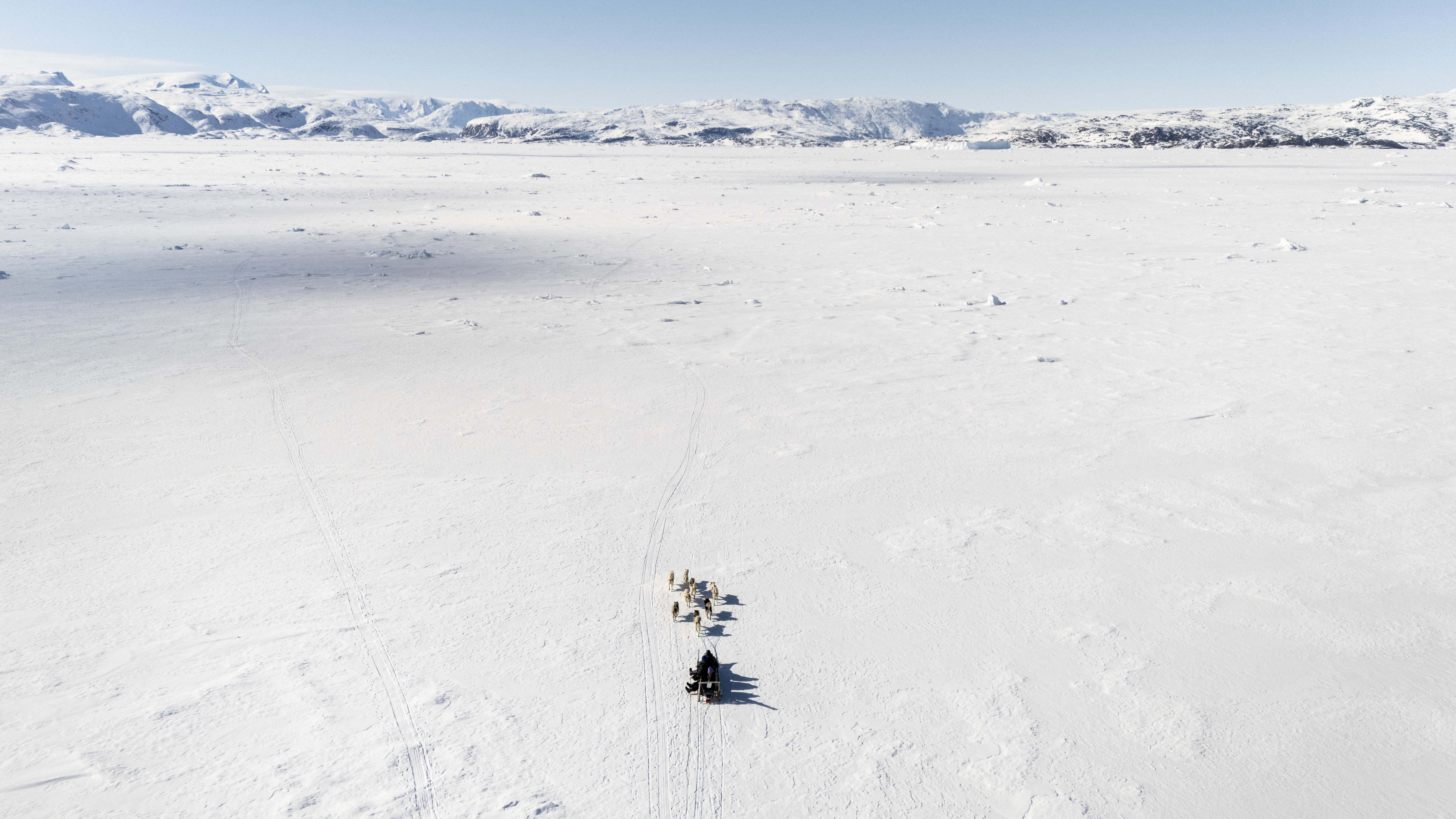Sled crossing over the frozen sea ice in the fjord from above.