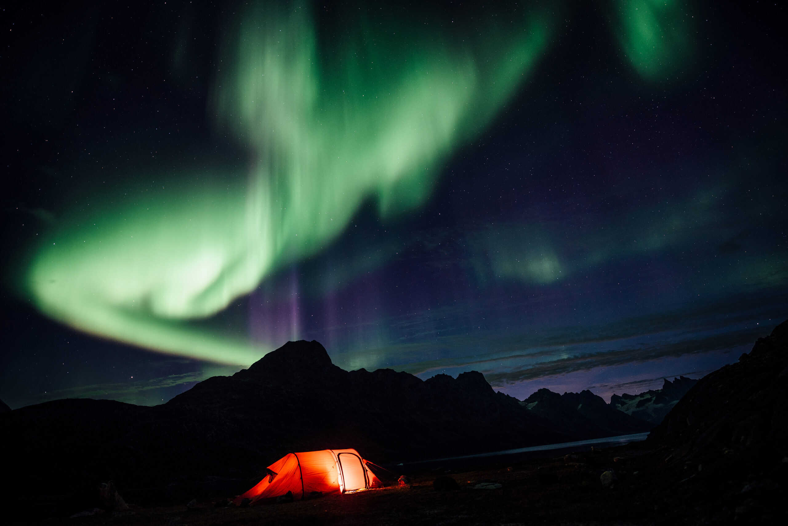 Northern lights over a lit tent, Camp In Tasiilaq Fjord