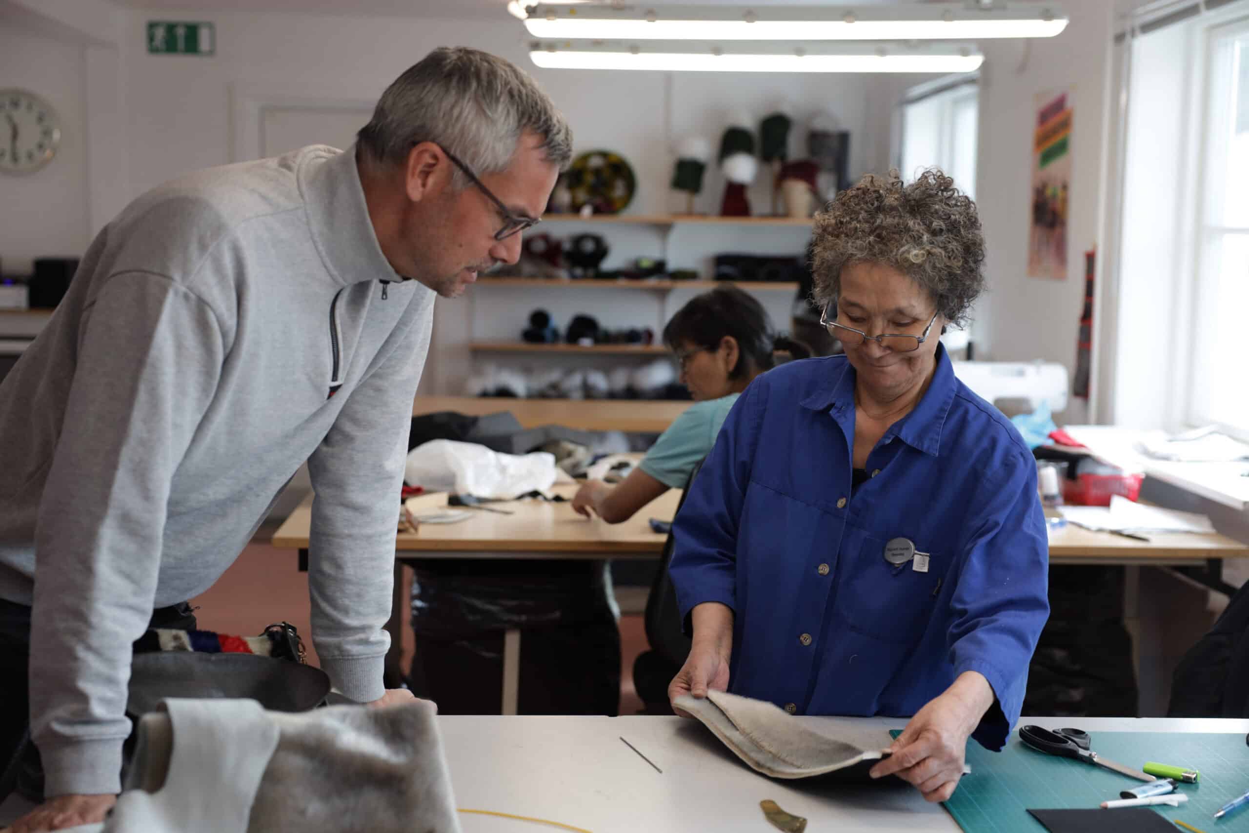 A woman showing her work progress to a curious tourist at the local sealskin sewing facility.