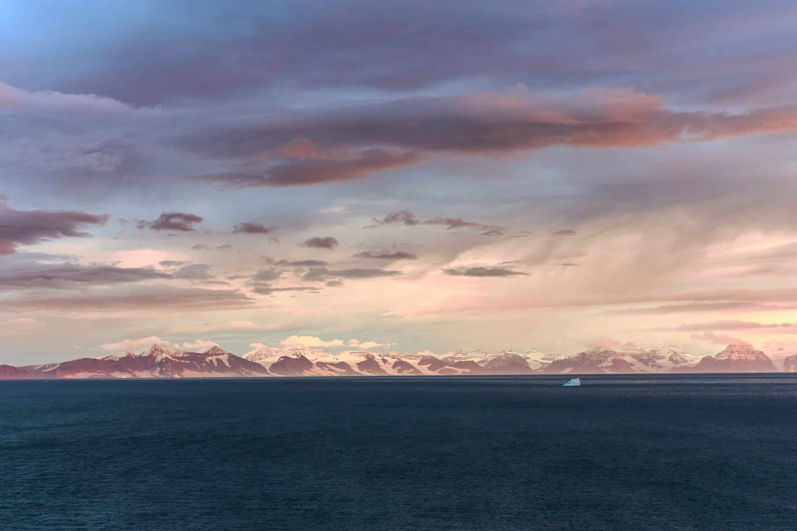 View from Ittoqqortoormiit over the fjord entrance, moody cloudy sky and snow covered mountain tops on the other side of the fjord.
