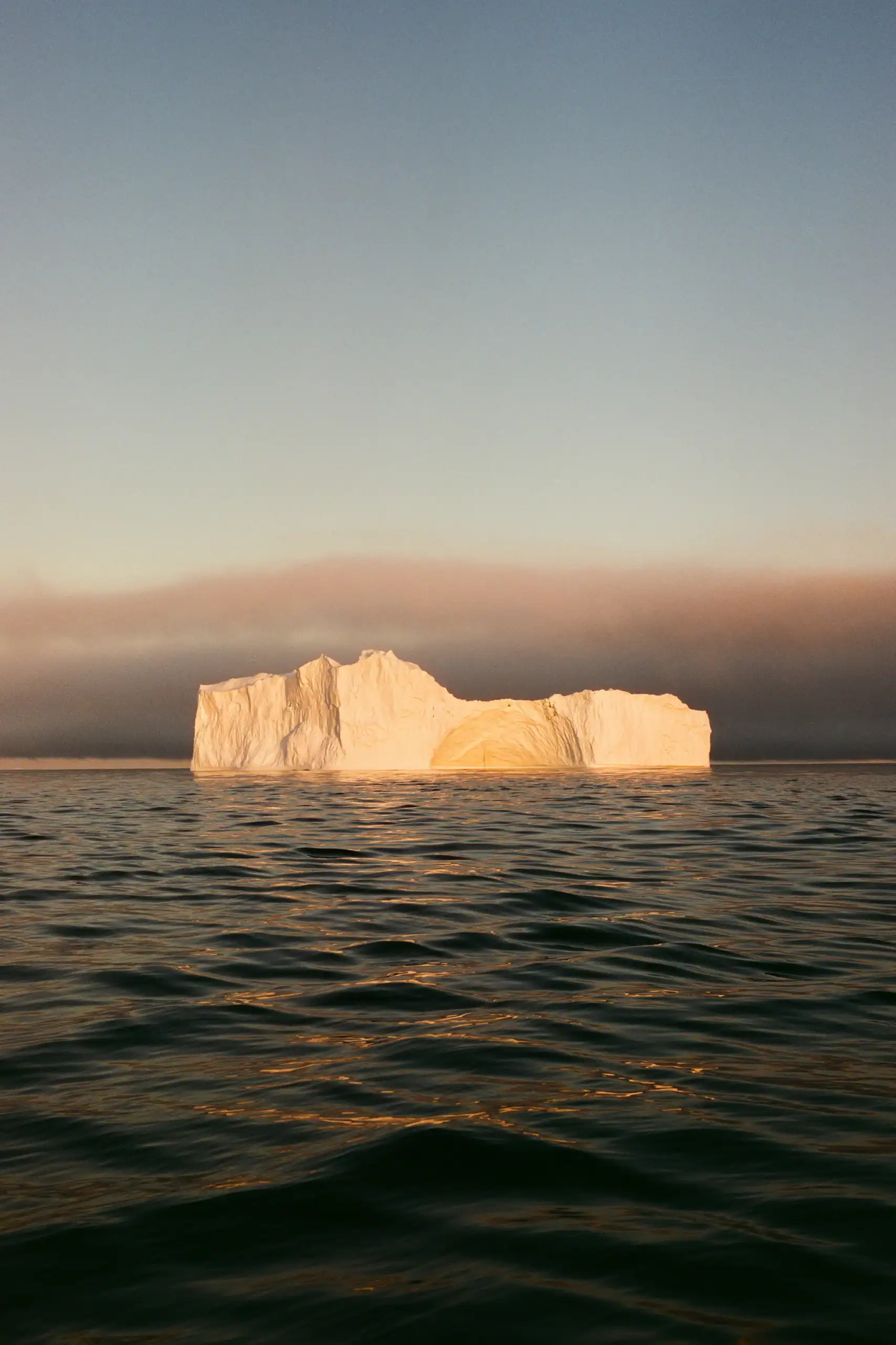 A giant iceberg floating in the still waters in the golden sun of September.