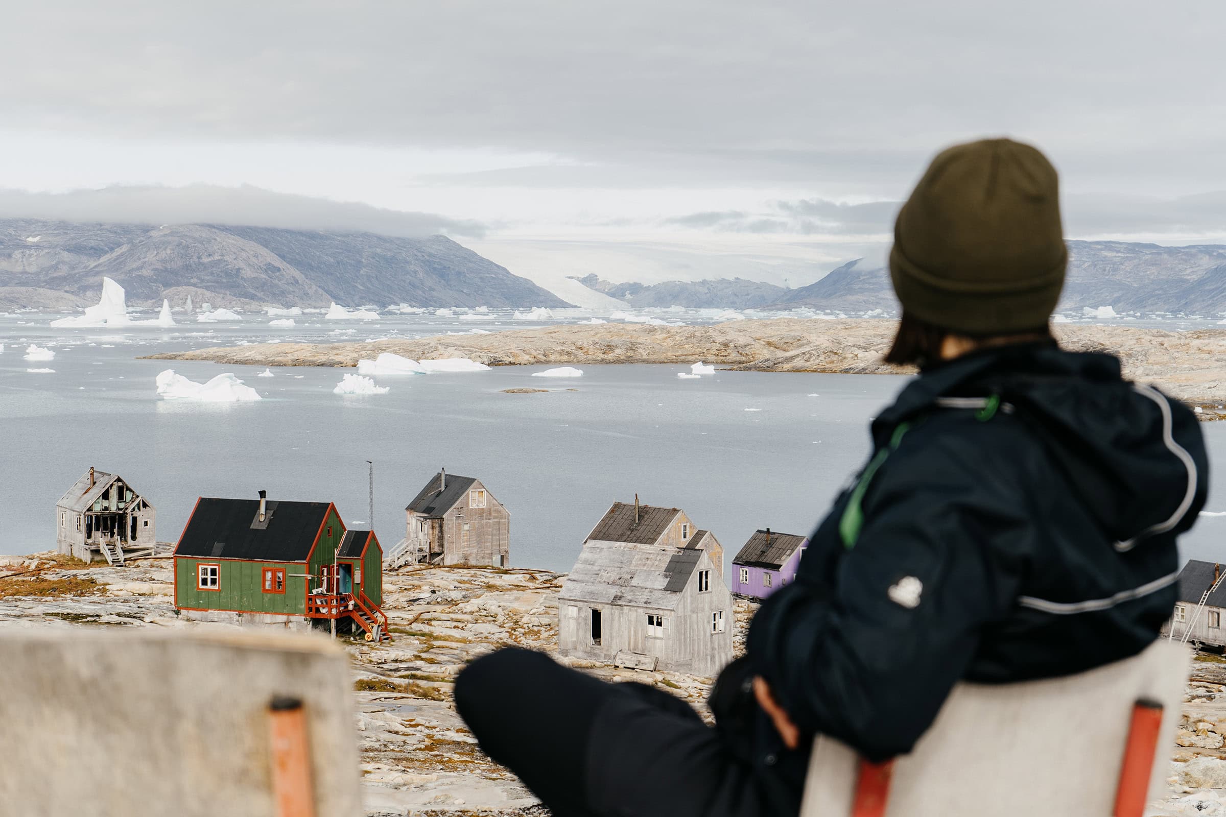 A person sitting on a chair overlooking the settlement of Isertoq with a view of the Greenland ice sheet in the distance.
