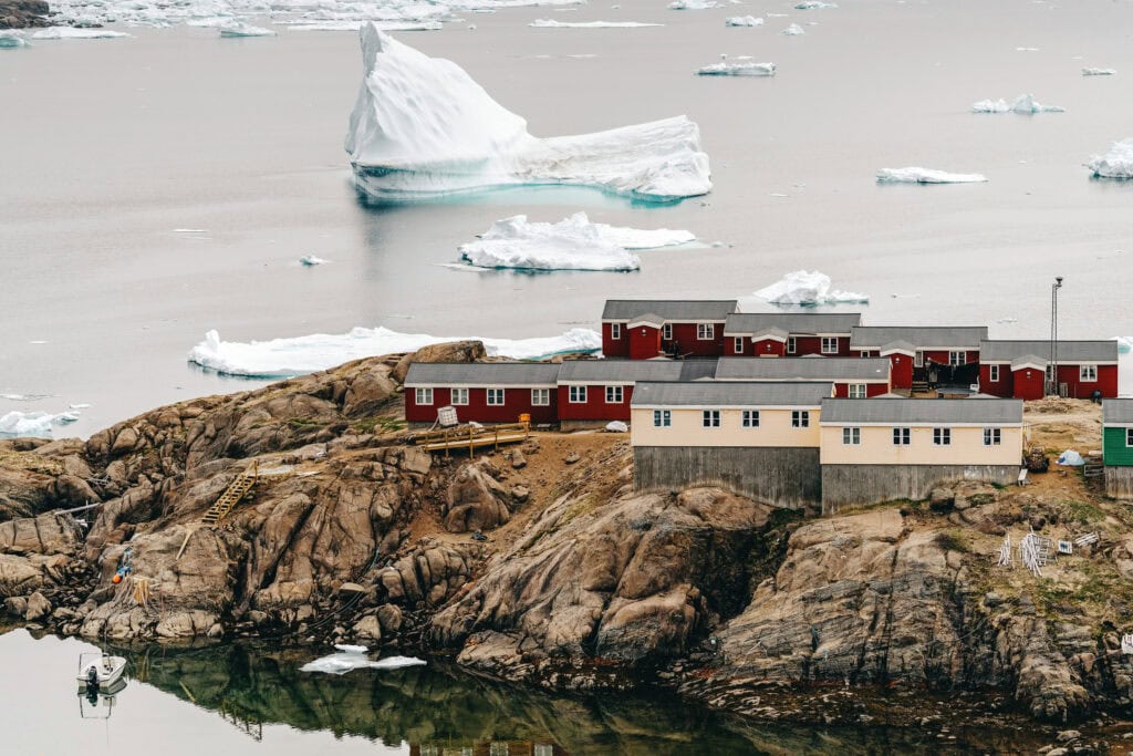 Red and white houses of Tasiilaq on the rocky shore with icebergs beyond