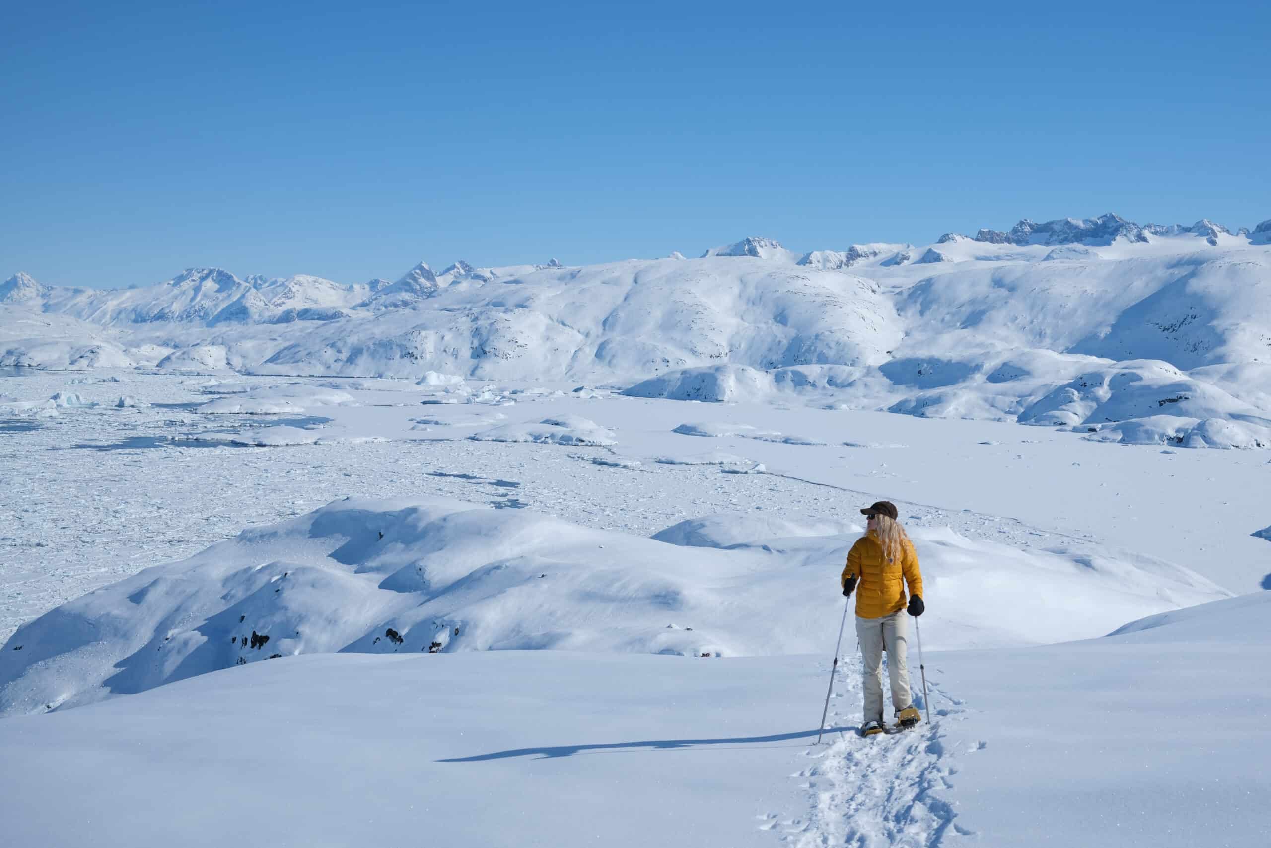 A tourist snowshoeing in the snow covered backcountry of Ammassalik Island overlooking Sermilik Fjord.