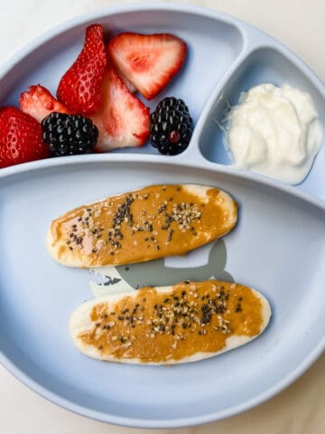 This is a photo of a baby led weaning friendly meal or snack. It contains baby teethers with peanut butter for fat, yogurt for protein and strawberries and blueberries for nutrients and fiber.