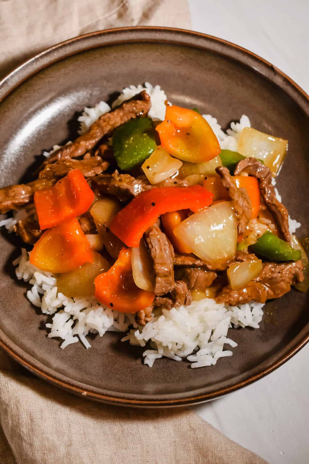 Close up picture of pepper steak stir fry served on top of rice.