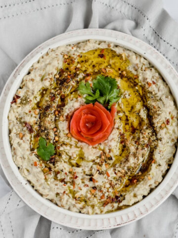 this is a photo of the baba ganoush eggplant dip from a top view with a tomato peel flower in the center along with olive oil and some red pepper flakes.