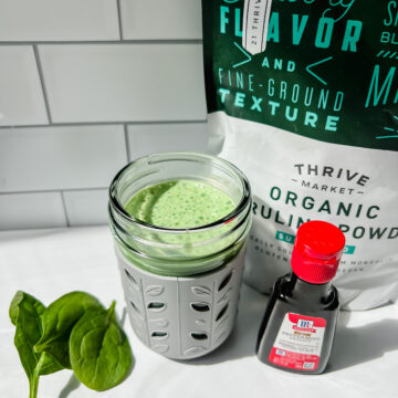 This is a photo of the healthy shamrock shake that's toddler and kid friendly in a small toddler sippy cup with the spirulina powder, spinach and peppermint extract on the side.