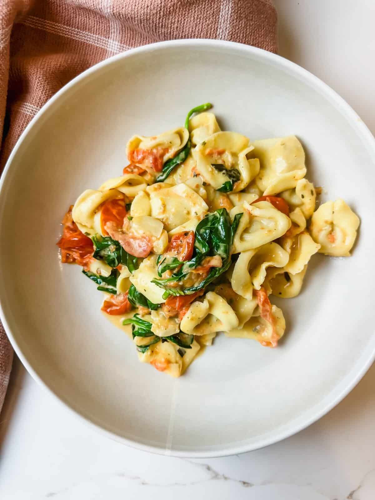 cloth draped on a countertop with a bowl of tortellini bake with tomatoes and boursin
