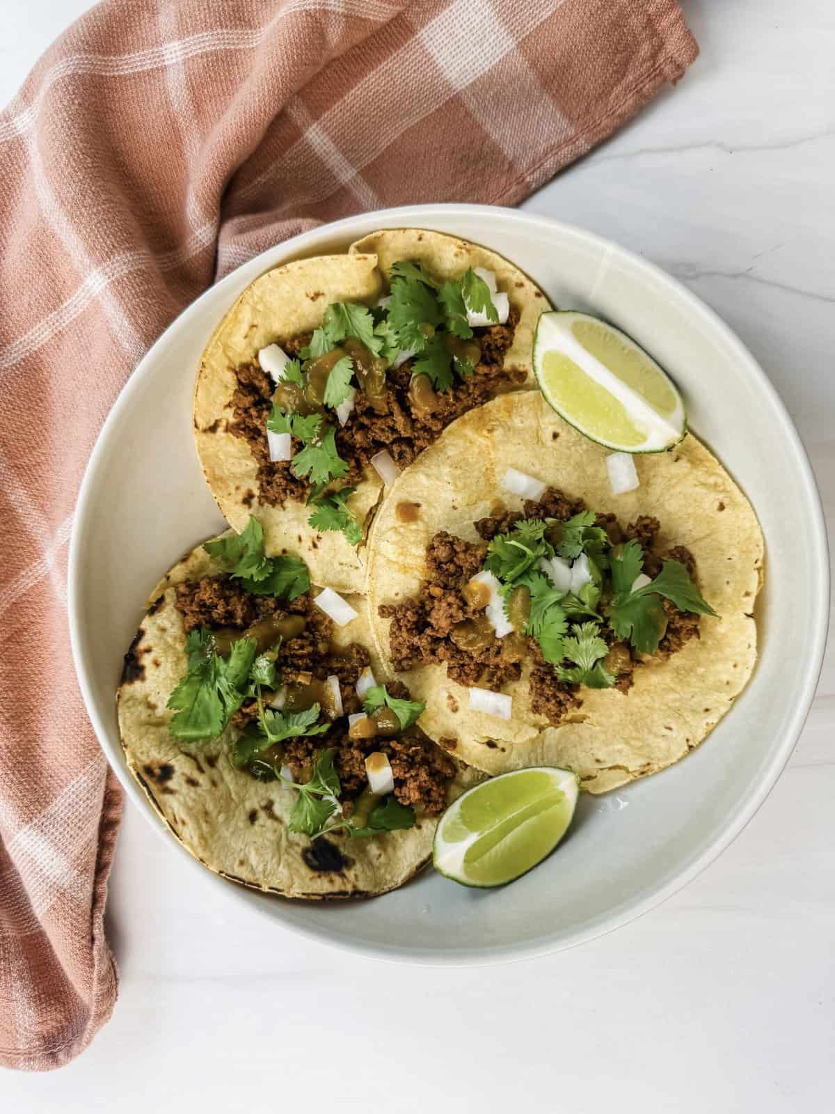 This is a top view of my easy ground beef street tacos on a plate topped with cilantro and onions and served with a wedge of lime. 