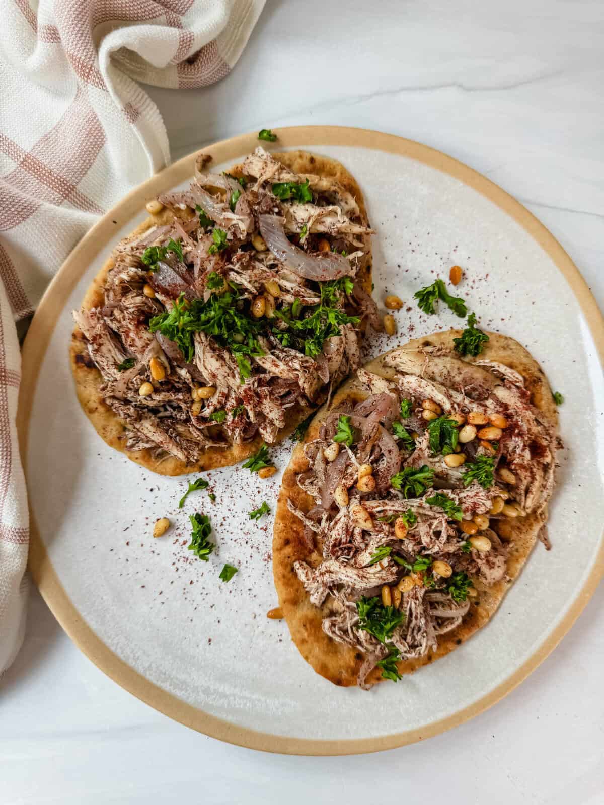 this is an overhead view of my chicken musakhan recipe. It shows naan topped with the caramelized onions with shredded chicken and garnished with toasted pine nuts and parsley 