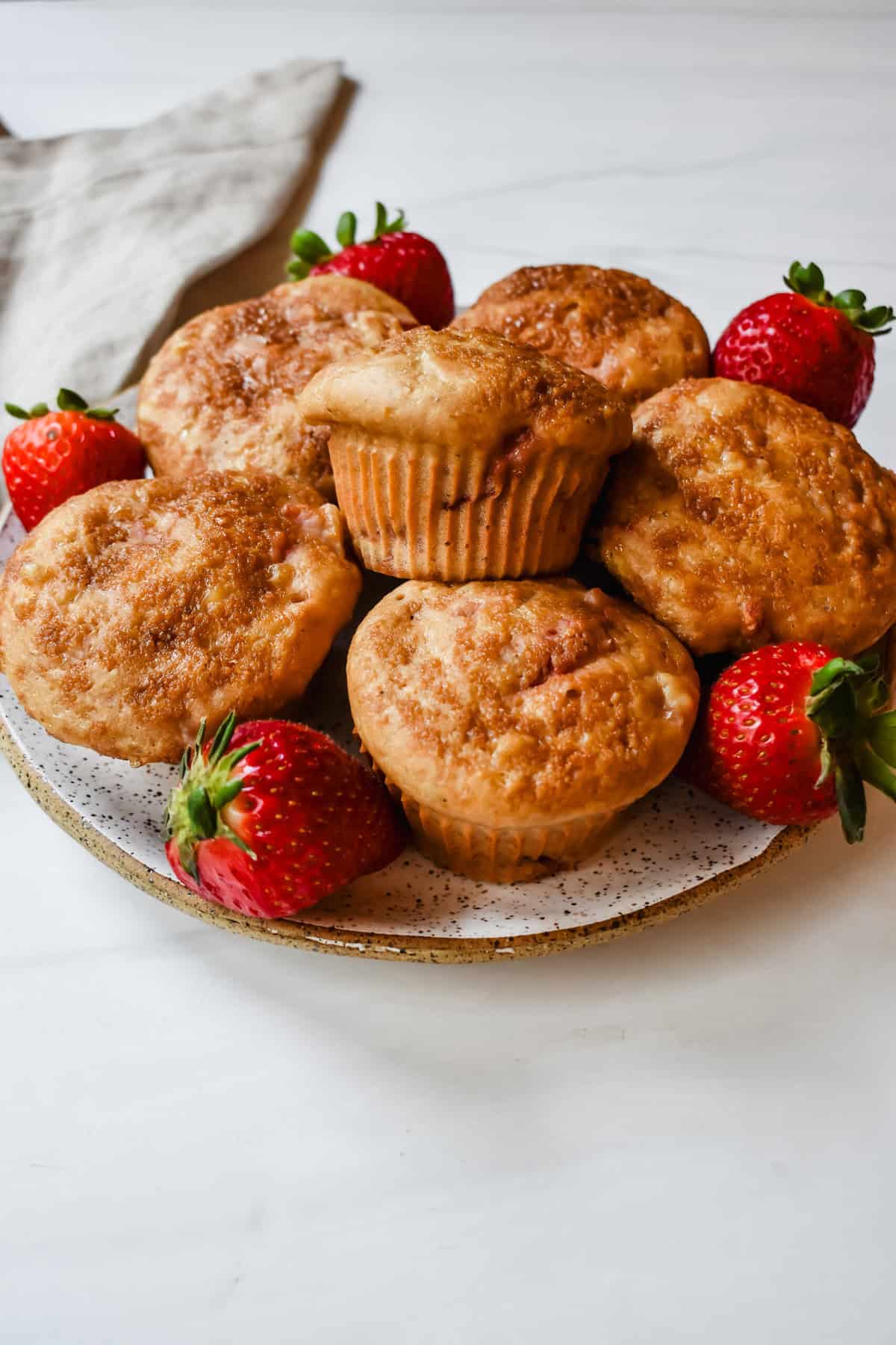This is a side view of my cottage cheese strawberry muffins on a plate with fresh strawberries. 