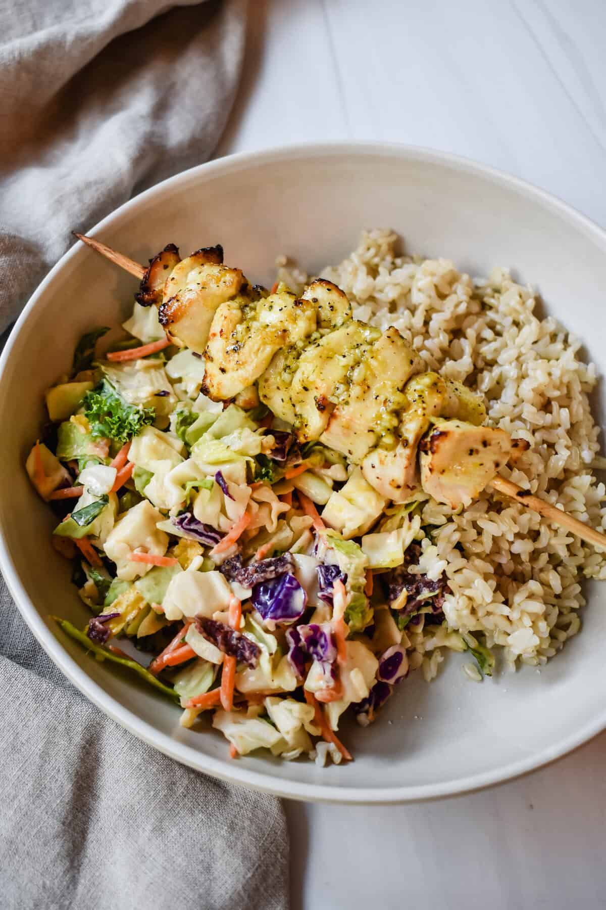 This is a side view close up of my lemon pepper chicken skewers on a bed of brown rice and salad. 