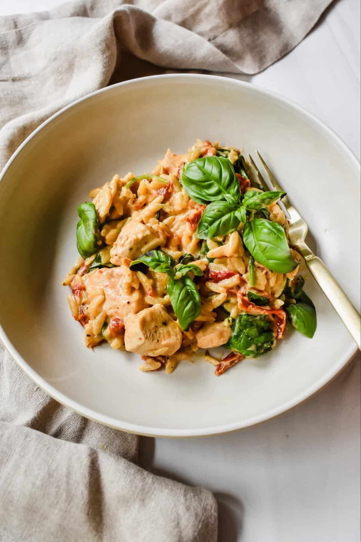 this is  a side close up of my one pot creamy lemon chicken orzo in a bowl with a golden fork. 