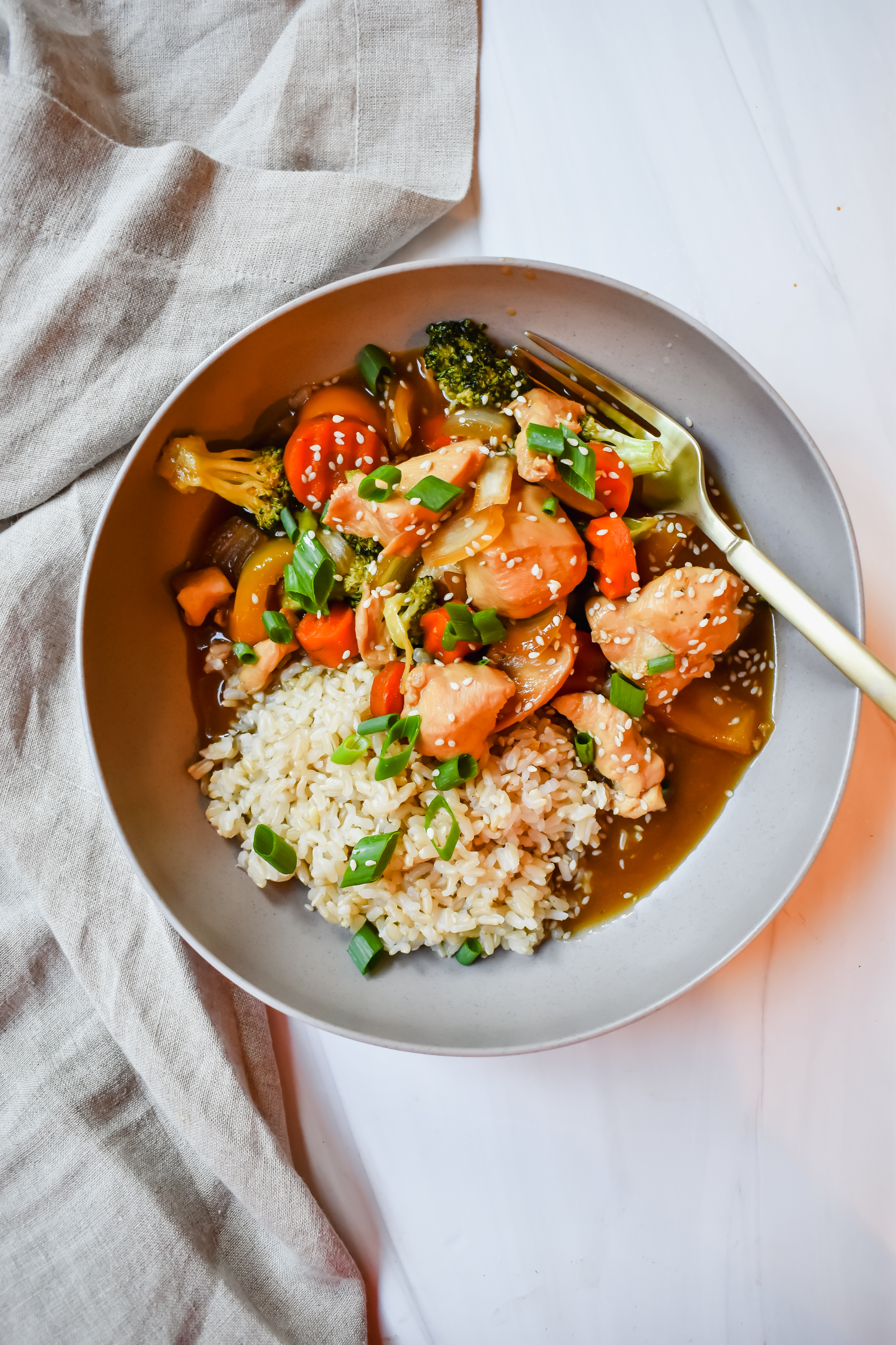 This is a top view of my slow cooker honey garlic chicken in a bowl served with rice and topped with sliced green onions and sesame seeds. 