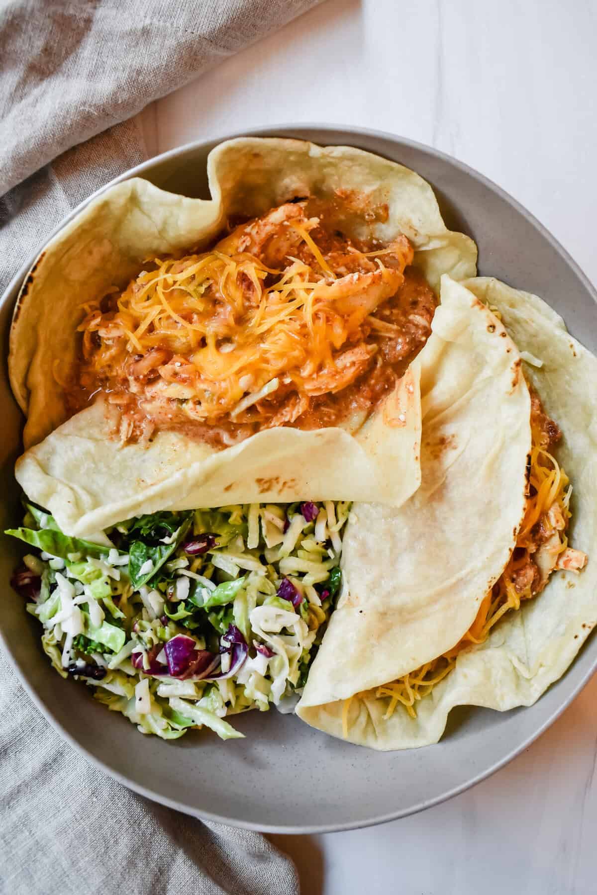 This is a top view of my creamy crock pot rotel chicken in a flour tortilla with low fat shredded cheese on top and served with a side salad in a plate.