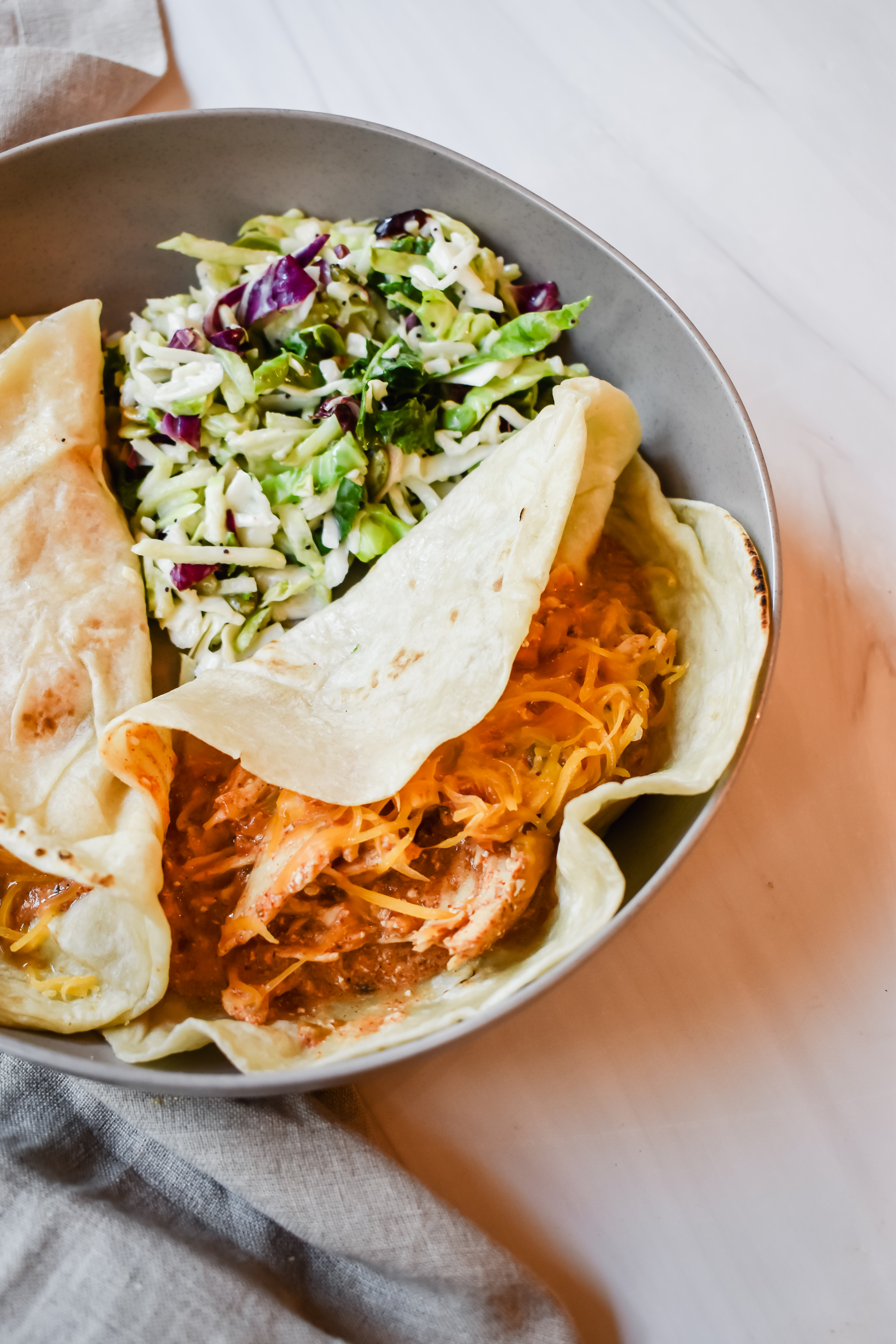 This is a side view of my creamy crock pot rotel chicken in a flour tortilla with low fat shredded cheese on top and served with a side salad in a plate.