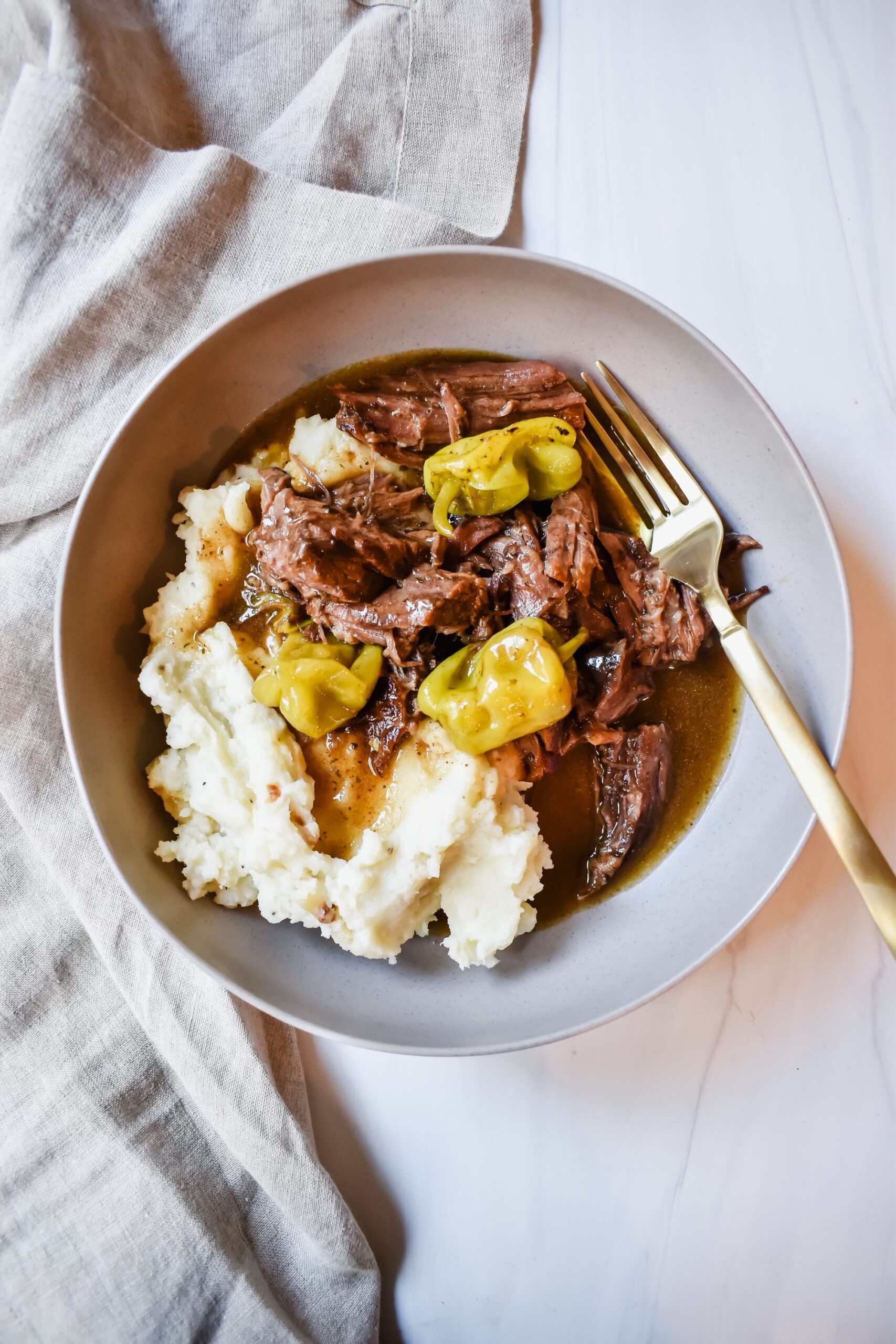 This is a top view of my healthy-ish Mississippi Pot roast served with some mashed potatoes with some peperoncinis on a plate. 