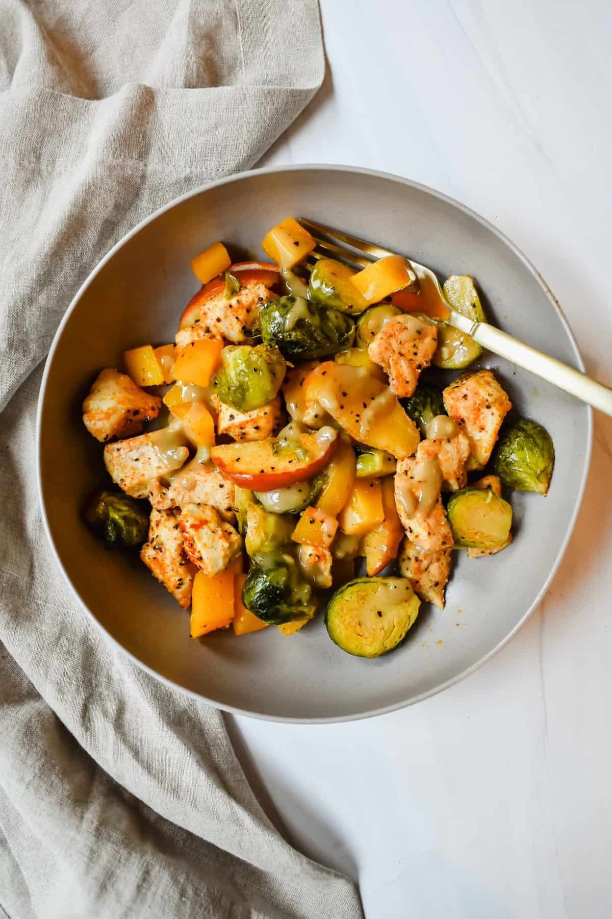 This is a top view of my fall sheet pan chicken and veggies dish which is topped with a honey tahini glaze and in a bowl. 