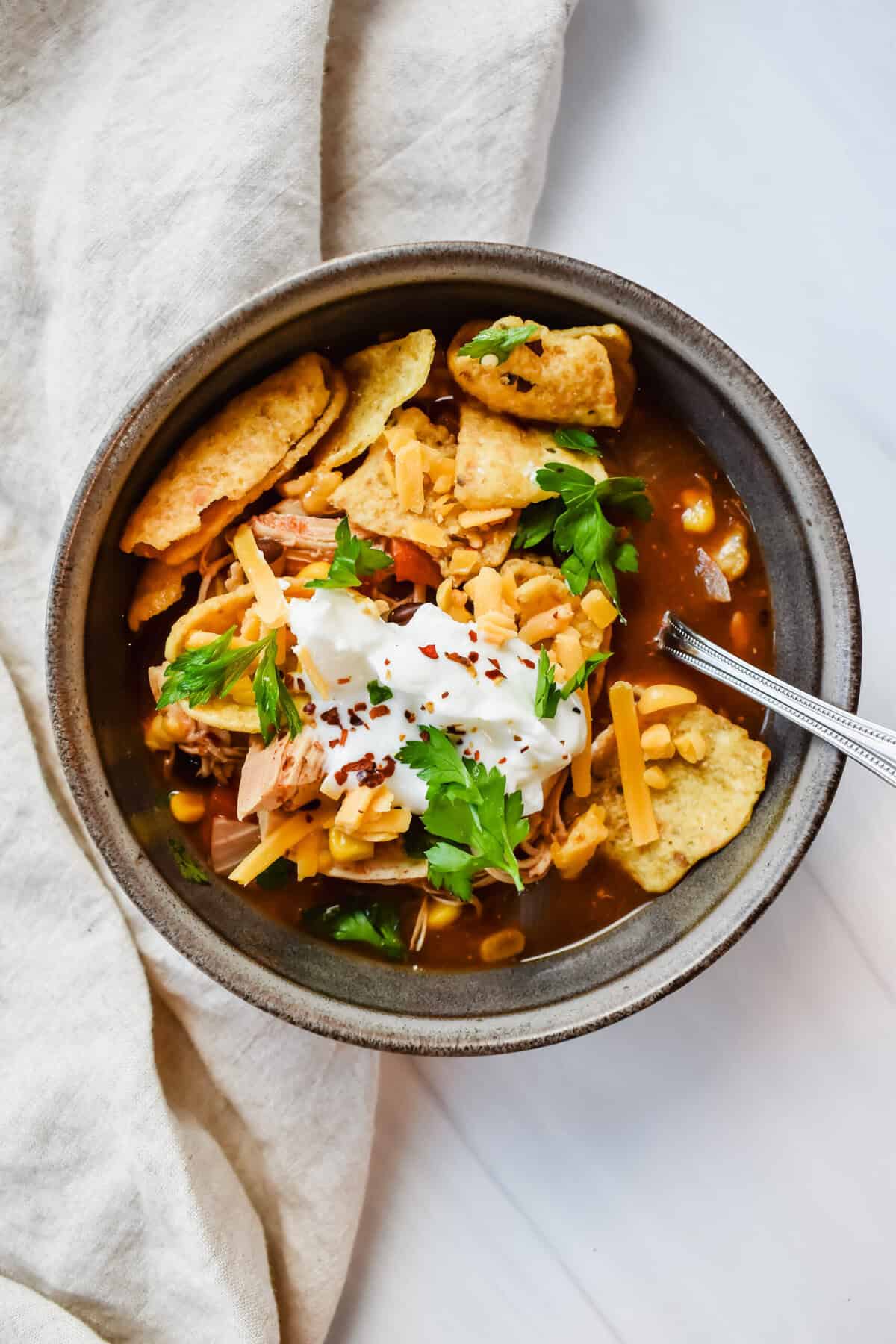 This is a top view of my crockpot southwest chicken soup in a bowl topped with corn chips, greek yogurt, mexican cheese and red pepper chili flakes.