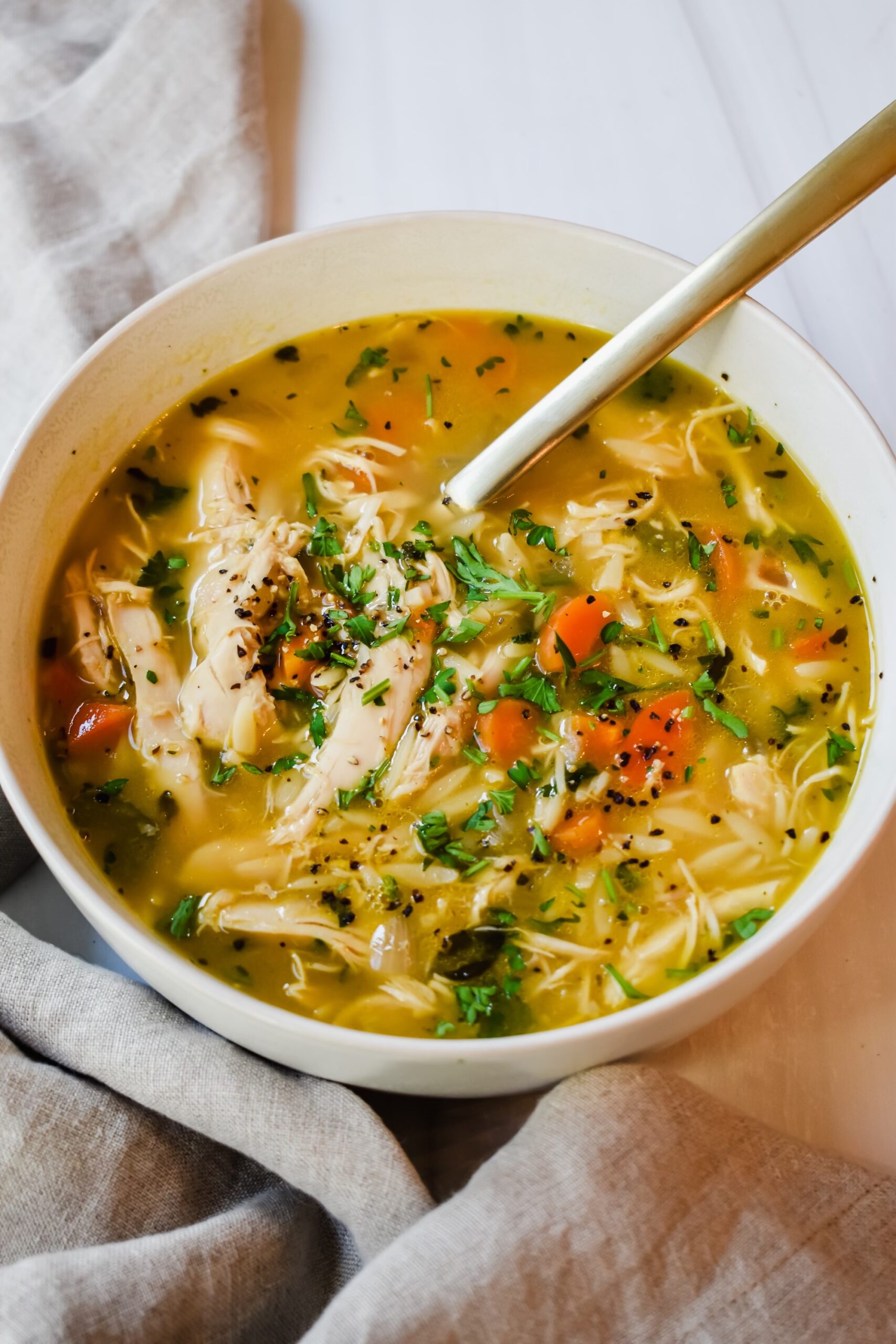 This is a top view of my greek chicken soup with lemon and orzo in a bowl with a golden spoon. 