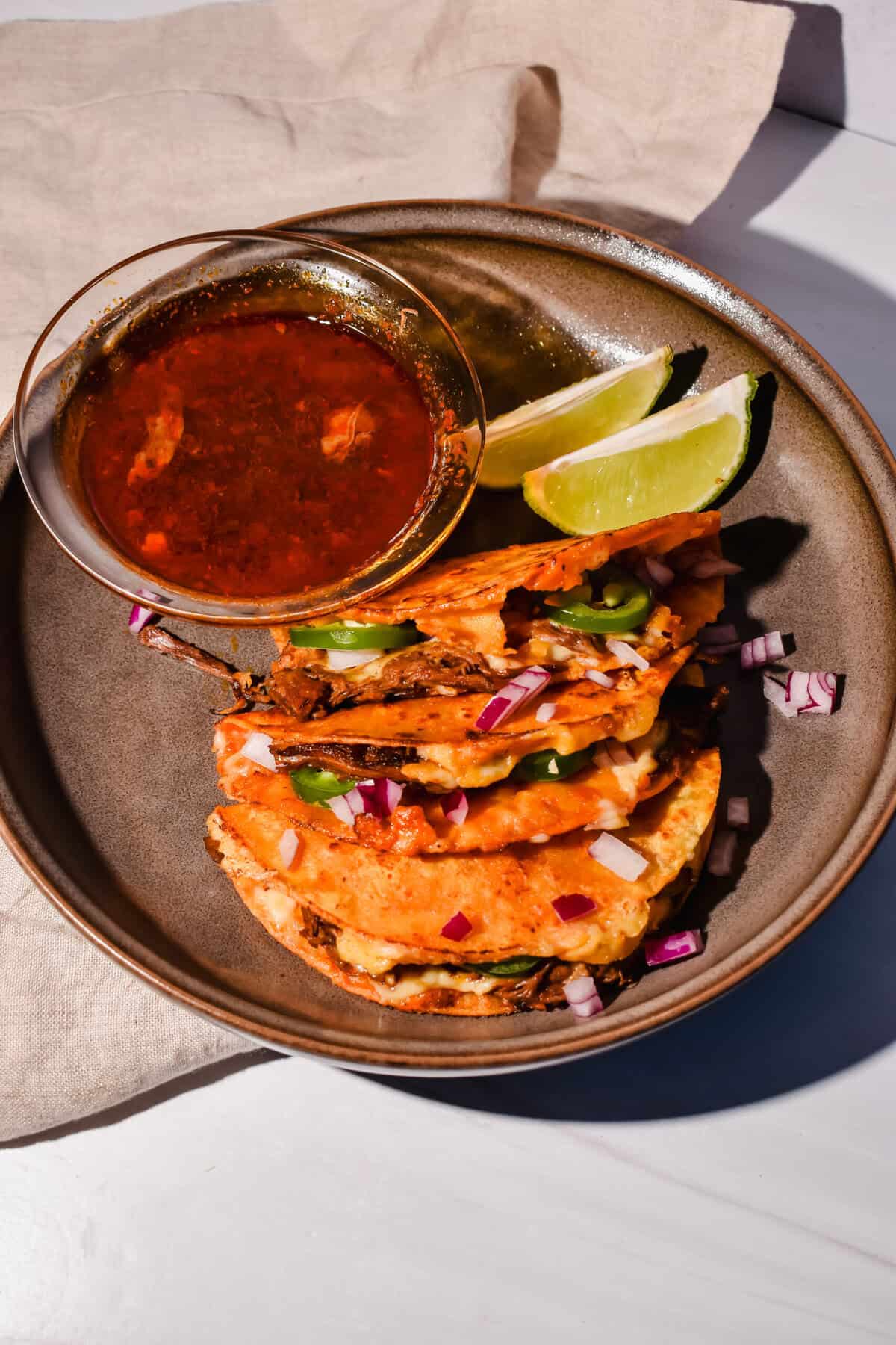 this is my easy birria bomb tacos on a plate with consume and lime 