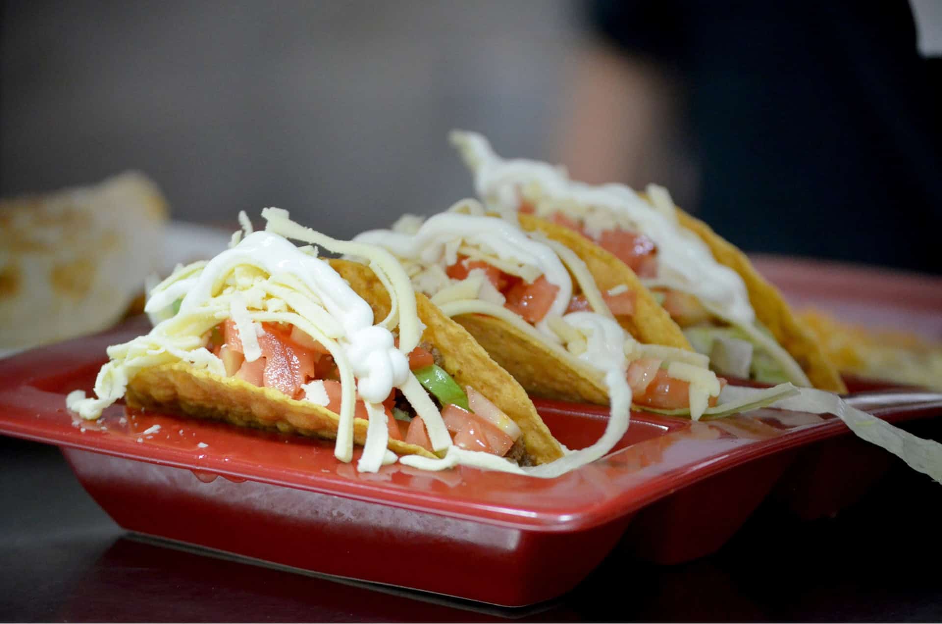 Tacos with fresh vegetables, cheese, and meat on a red plate.