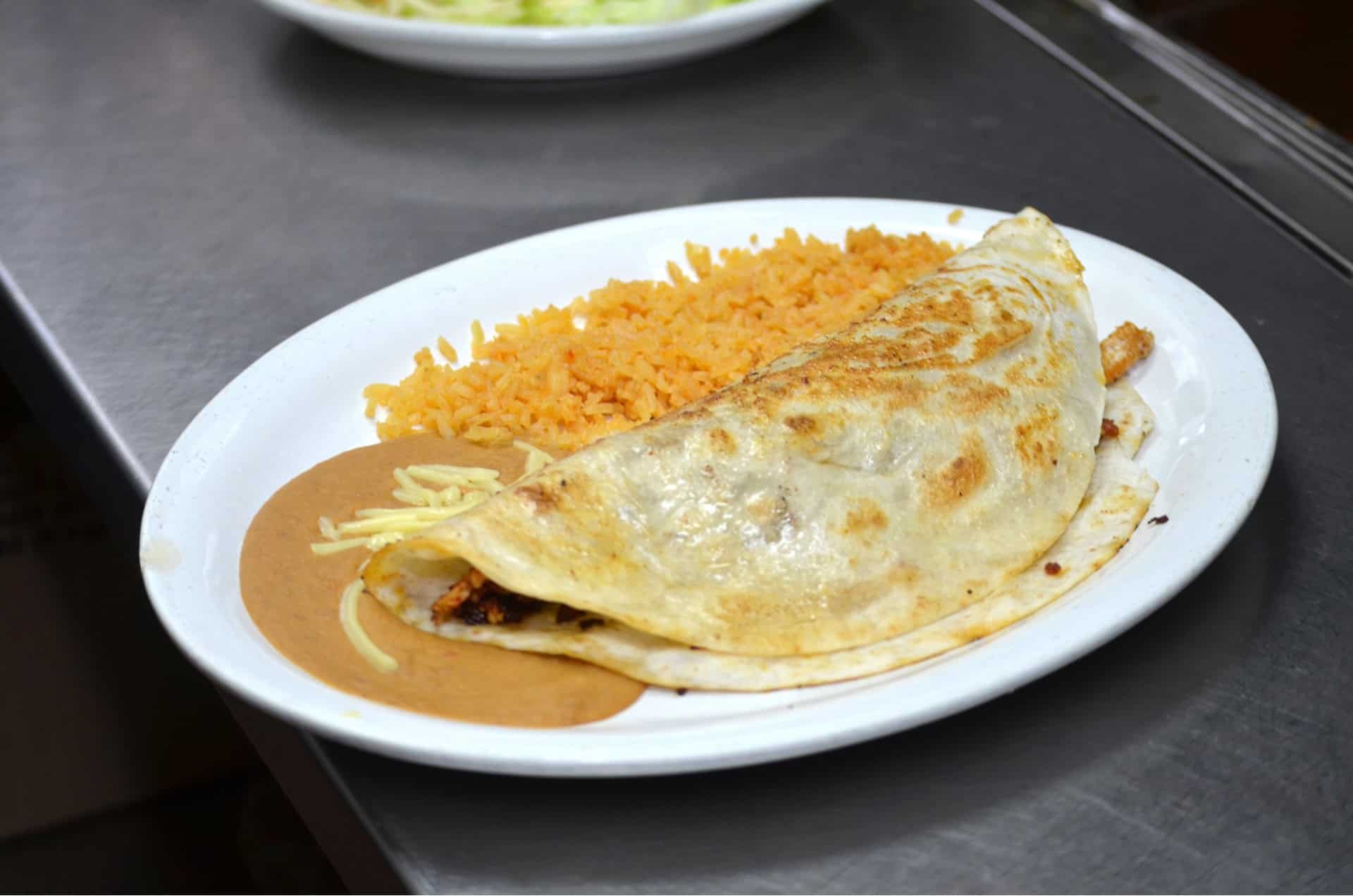 Enchilada with melted cheese served with flavorful Mexican rice on a white plate.