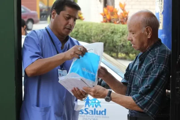Foto reciente de una persona mayor recibiendo medicamentos en su domicilio, con logo de EsSalud visible.