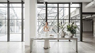Bride in elegant wedding dress holding a magazine in modern industrial venue.