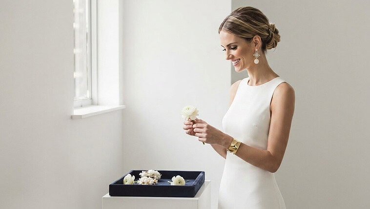 Elegant bride in white dress looking out window, bridal jewelry, minimalistic setting.