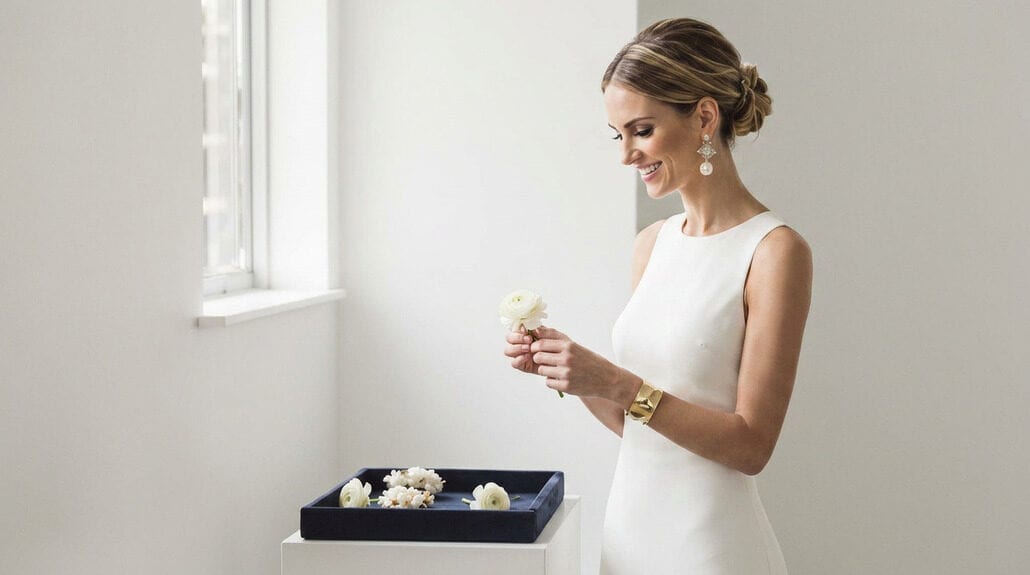 Elegant bride in white dress looking out window, bridal jewelry, minimalistic setting.