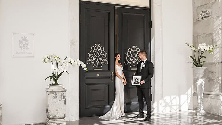 Bride and groom outside historic venue with elegant black doors and floral decor.