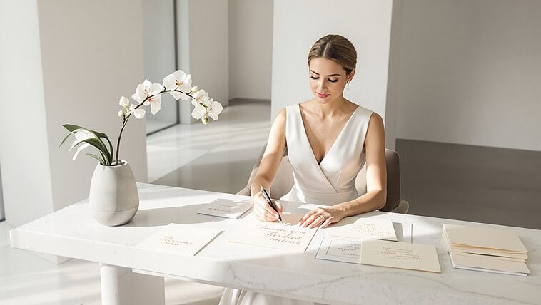 Elegant woman planning wedding at a bright, modern office desk with wedding documents and a white or.