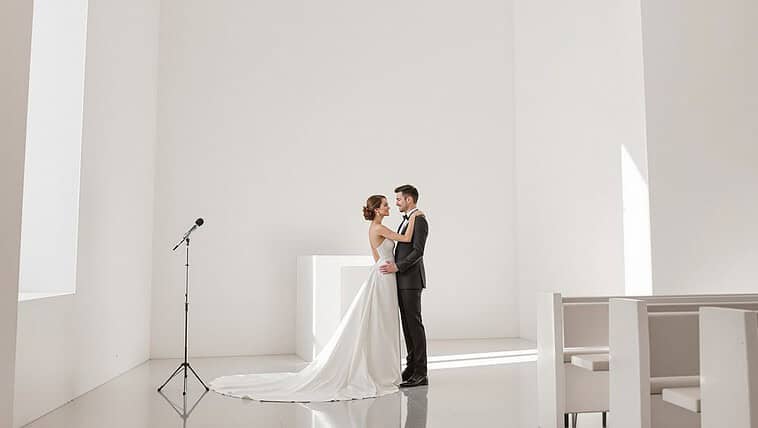 Bride and groom sharing a kiss in a simple, modern wedding venue with white walls and natural light.