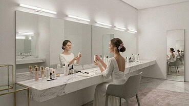 Bride applying makeup in a modern bathroom with a large illuminated mirror.