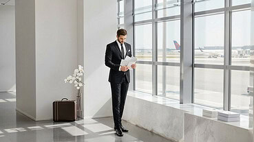 Bride in wedding dress waiting at airport terminal with suitcase.