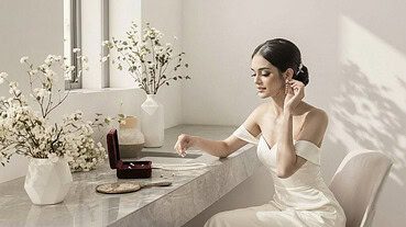 Bride in elegant wedding dress holding pearl necklace by window.