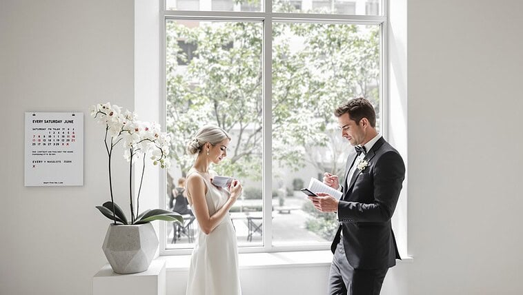 Elegant wedding ceremony with bride and groom reading vows by a large window.