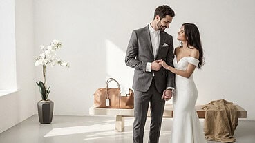 Bride in elegant white wedding gown and groom in tailored gray suit with bow tie.